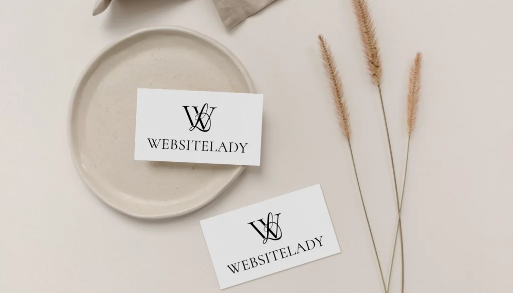 wordpress-websites-professionell-webdesignerin-aus-berlin Zwei Visitenkarten mit dem Logo und Schriftzug "WEBSITELADY" liegen auf einer beigen, minimalistischen Oberfläche. Eine Karte liegt auf einem hellen Keramikteller, daneben liegen getrocknete Gräser.