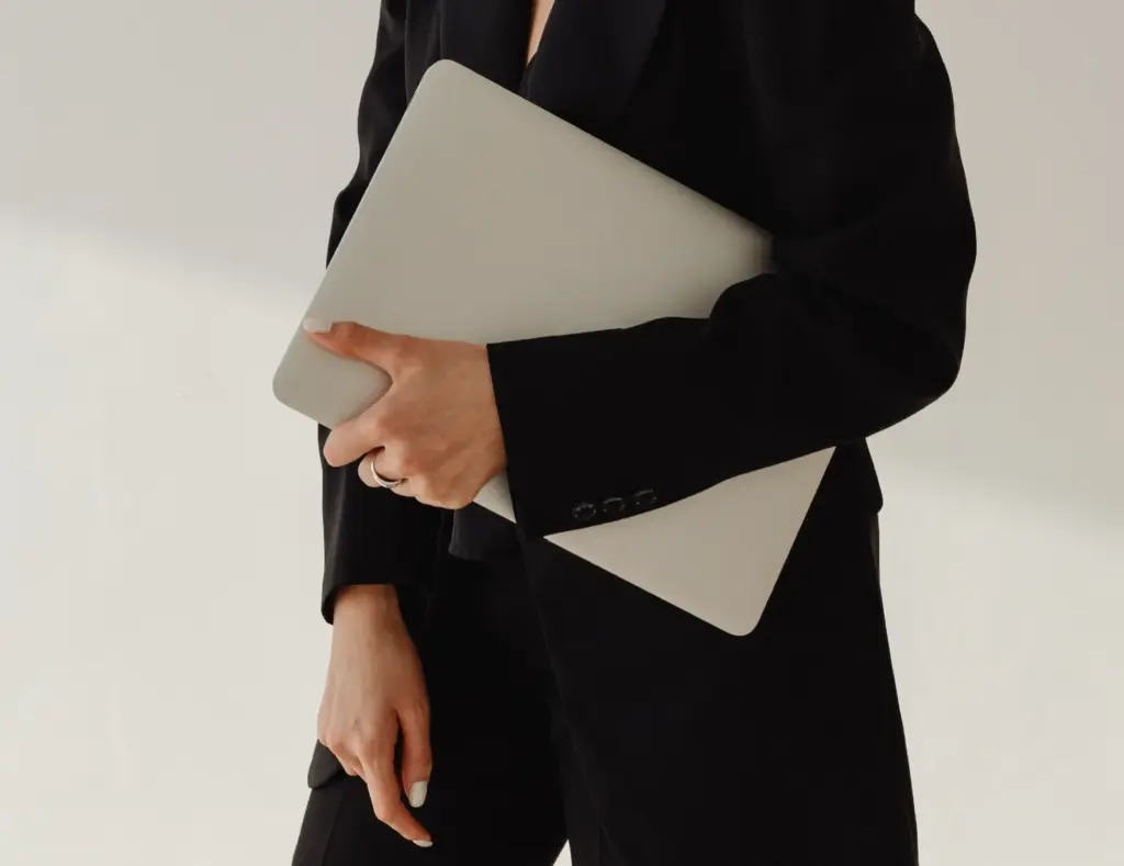 Eine Frau im schwarzen Anzug hält einen silbernen Laptop. Sie ist eine professionelle Webdesignerin für WordPress Websites.